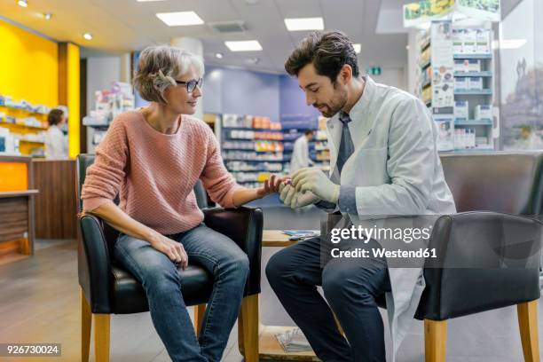 pharmacist measuring blood sugar of customer in pharmacy - pharmacist and patient stock pictures, royalty-free photos & images