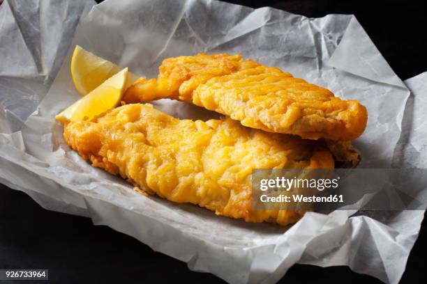 fried coalfish filet and lemon slices on greaseproof paper - dried fish stock-fotos und bilder