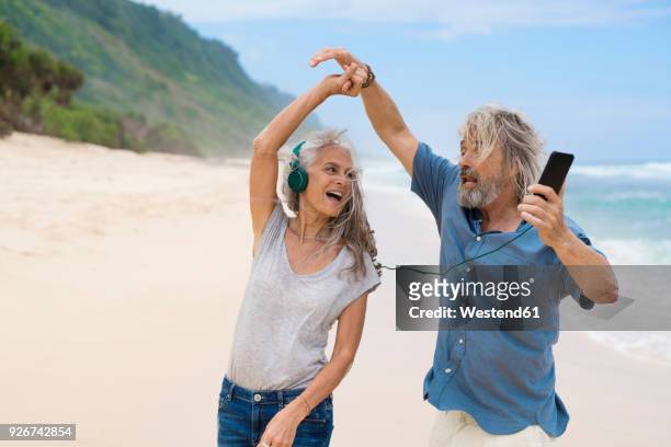handsome senior couple with headphones dancing on the beach - alter mann jung geblieben stock-fotos und bilder