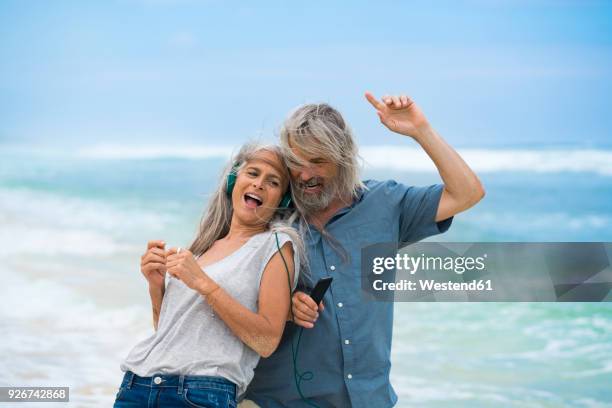 handsome senior couple with headphones dancing on the beach - bali dancing stock pictures, royalty-free photos & images