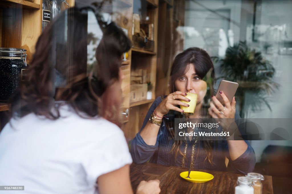 Woman with friend in a cafe holding smartphone and drinking coffee