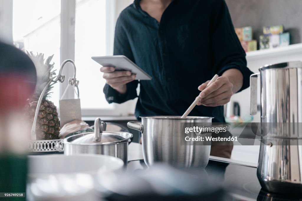 Man standing in kitchen reading news on his digital tablet while cooking