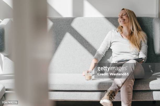 smiling woman relaxing on couch with laptop - tranquility stock-fotos und bilder