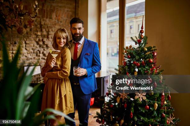 portrait of elegant couple with drinks at christmas tree - cocktail dress stock-fotos und bilder