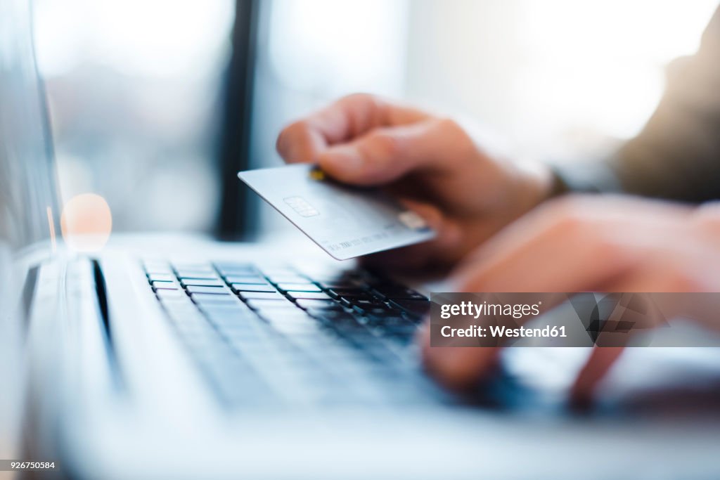 Man using laptop and holding credit card, close-up