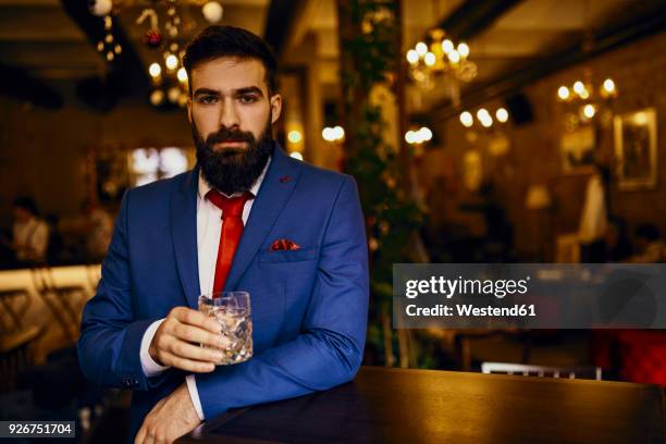 portrait of elegant young man in a bar holding tumbler - leaning on bar photos et images de collection