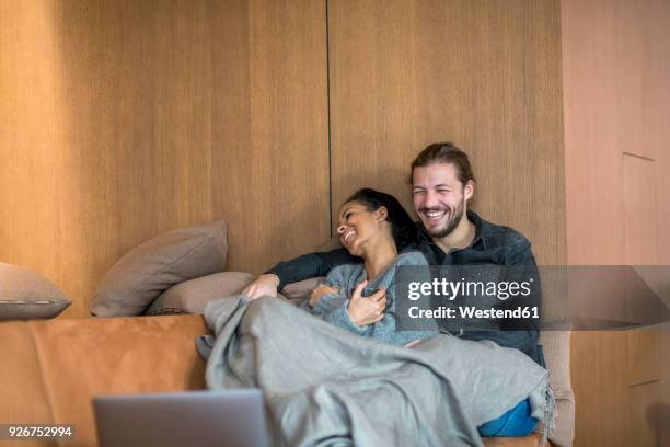 laughing young couple relaxing together on the couch - financial wellbeing stock pictures, royalty-free photos & images