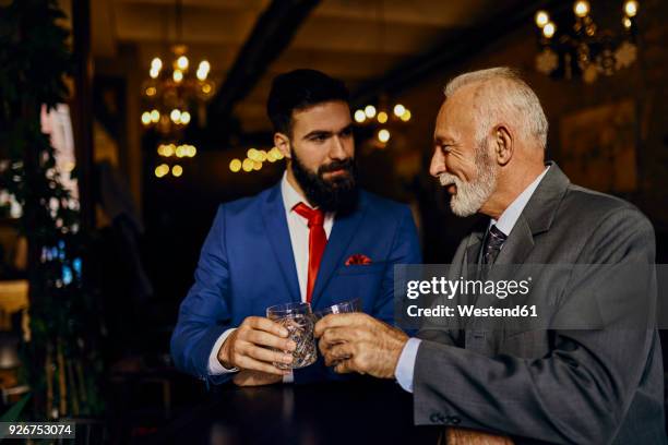 two elegant men in a bar clinking tumblers - whisky bar stockfoto's en -beelden