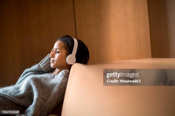 portrait of relaxed young woman listening music with headphones on couch - junge frau allein stock-fotos und bilder