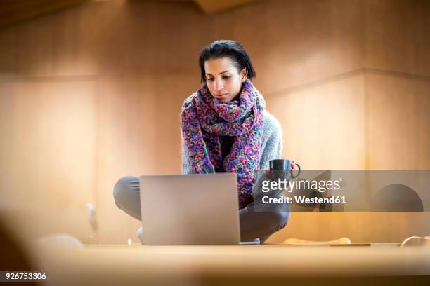 portrait of fashionable young woman with cup of coffee sitting on conference table using laptop - ambient light stock pictures, royalty-free photos & images