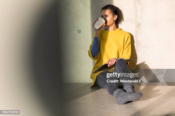 young woman wearing yellow pullover sitting on the floor drinking coffee to go - school stockings stock pictures, royalty-free photos & images