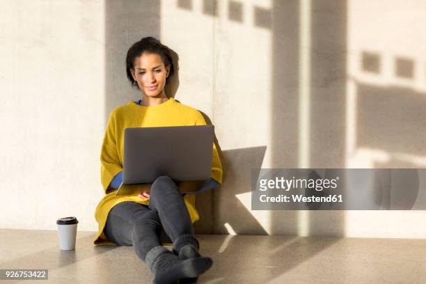 portrait of smiling young woman sitting on the floor using laptop - person in education stock-fotos und bilder