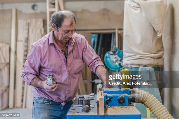 the senior 60-years-old man, carpenter and sashman, craftsman, working with the industrial milling machine at the small wood factory - 60 69 years imagens e fotografias de stock