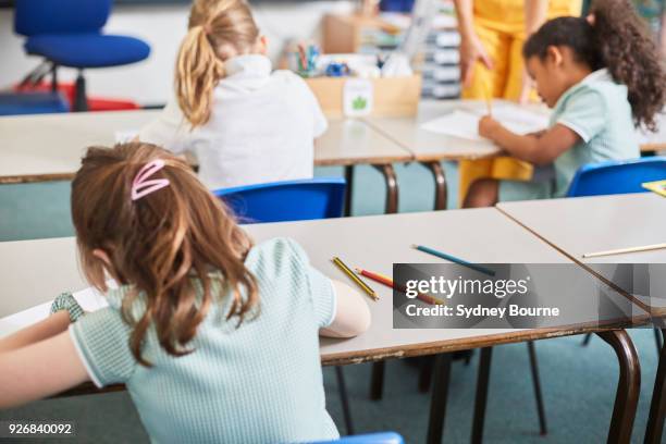 schoolgirl writing at classroom desk in primary school lesson, rear view - grundskoleelev bildbanksfoton och bilder