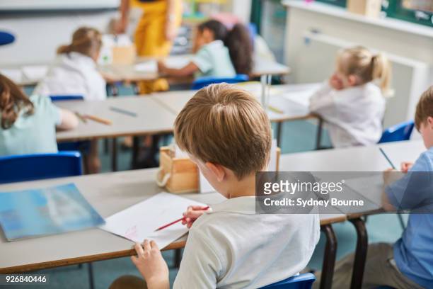 primary schoolboy and girls doing schoolwork at classroom desks, rear view - uk stock pictures, royalty-free photos & images