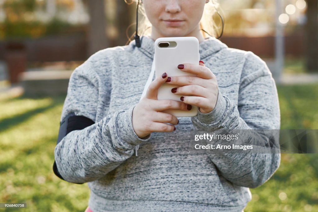 Young woman training in park looking at smartphone, cropped