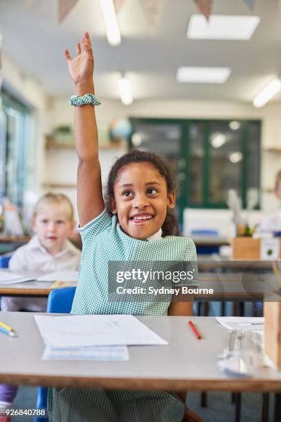 schoolgirl with hand up in classroom at primary school - 5-10 2016 stock pictures, royalty-free photos & images