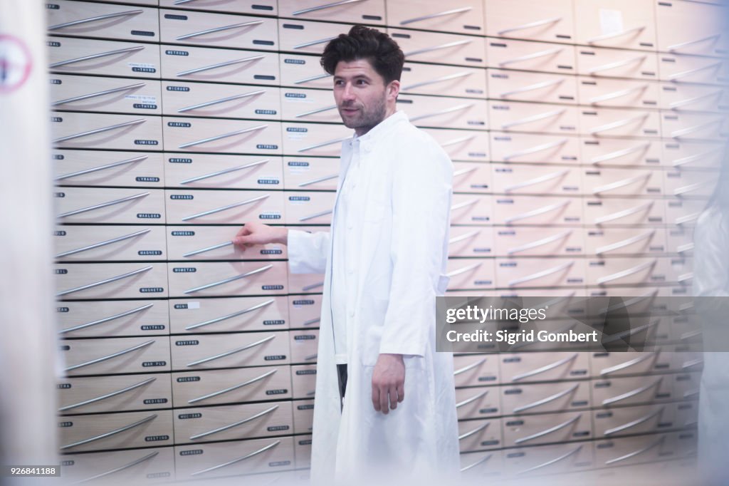 Young male pharmacist standing by pharmacy drawers
