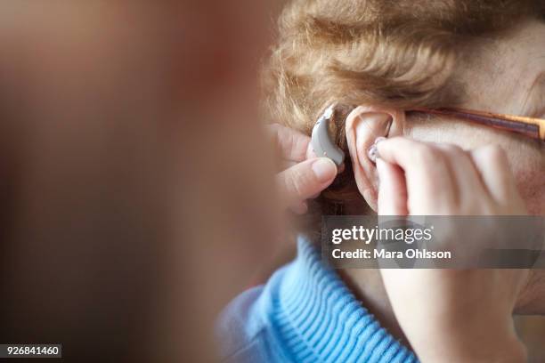 mature woman helping senior woman insert hearing aid, close-up, differential focus - prothèse auditive photos et images de collection