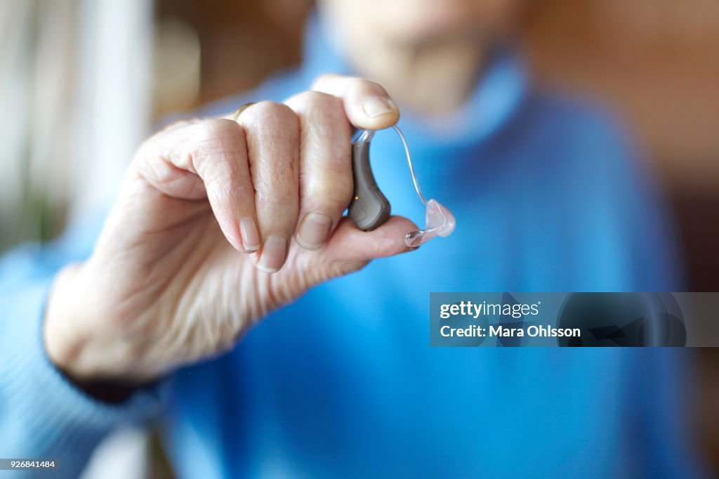 Senior woman holding hearing aid, close-up