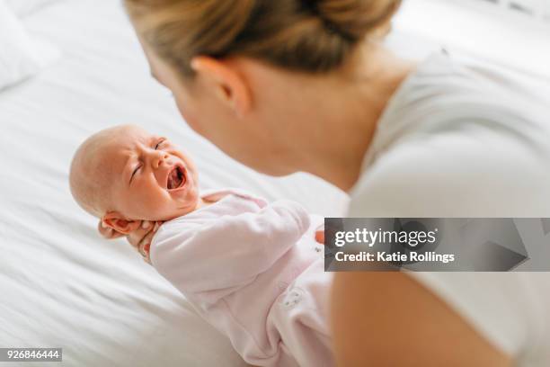 young woman cradling crying baby daughter on bed, over shoulder view - moms crying in bed stock pictures, royalty-free photos & images