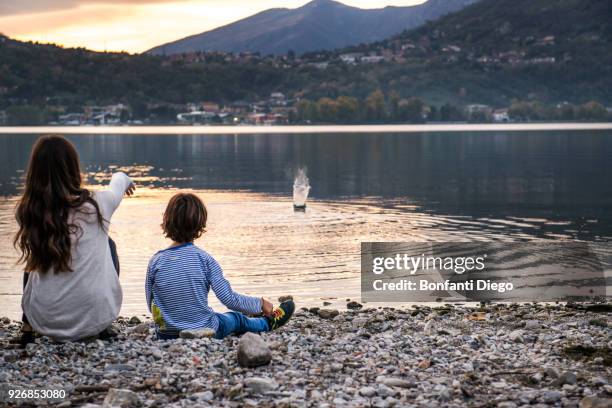 rear view of boy and young woman throwing pebbles into river at dusk, vercurago, lombardy, italy - vercurago stock pictures, royalty-free photos & images