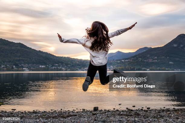 rear view of young woman jumping mid air by river at dusk, vercurago, lombardy, italy - vercurago stock pictures, royalty-free photos & images