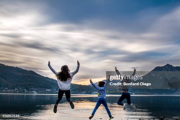 rear view of boy and young women jumping mid air by river at dusk, vercurago, lombardy, italy - vercurago stock pictures, royalty-free photos & images