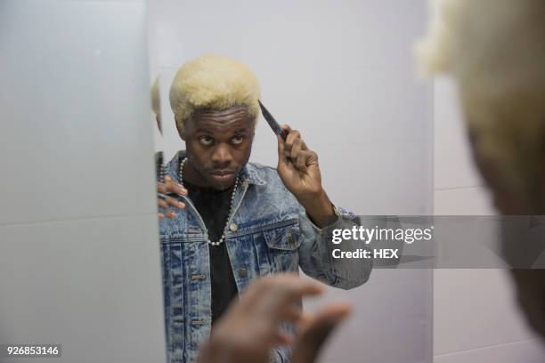 a young man getting ready in the mirror - bleached hair - fotografias e filmes do acervo
