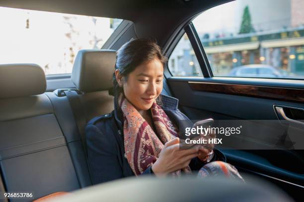 young asian businesswoman looking at smartphone sitting in car service limousine - taxi - fotografias e filmes do acervo