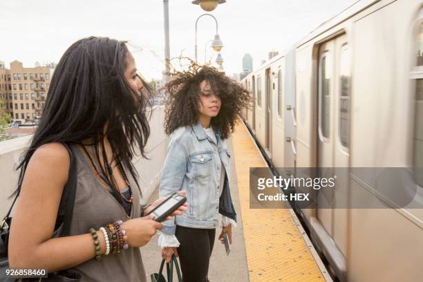 young women waiting at a train station in queens, new york - queens stad new york stock-fotos und bilder