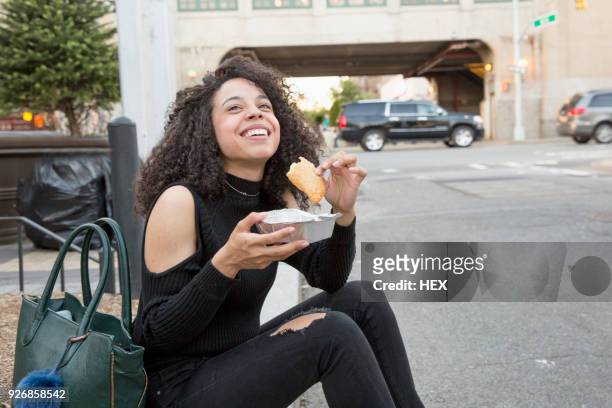 young woman eating outside a grocery store in queens, new york - queens stockfoto's en -beelden