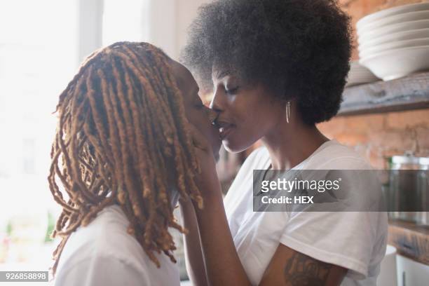 lesbian couple kissing in their kitchen - black lesbians kiss stock pictures, royalty-free photos & images