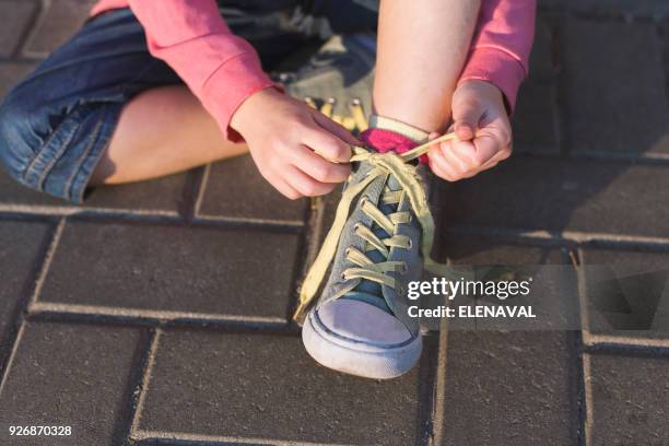 girl sitting on ground tying her shoelaces - shoelace stock-fotos und bilder