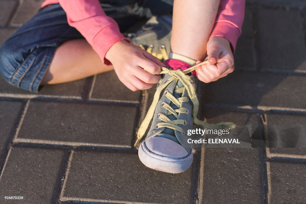 Girl sitting on ground tying her shoelaces