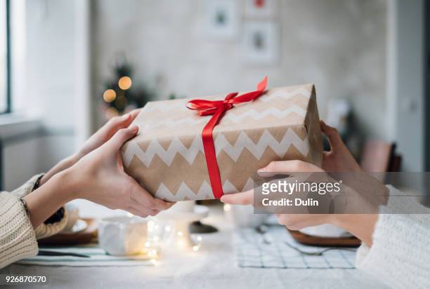 woman giving her friend a wrapped christmas gift - anbieten stock-fotos und bilder