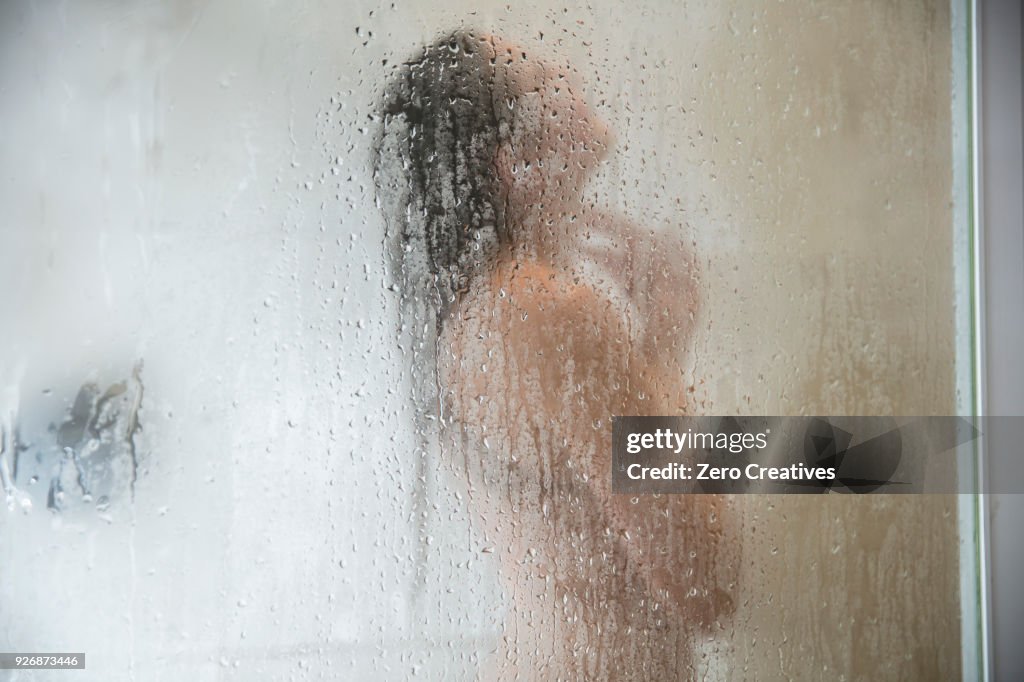 Young woman in shower behind steamed glass door
