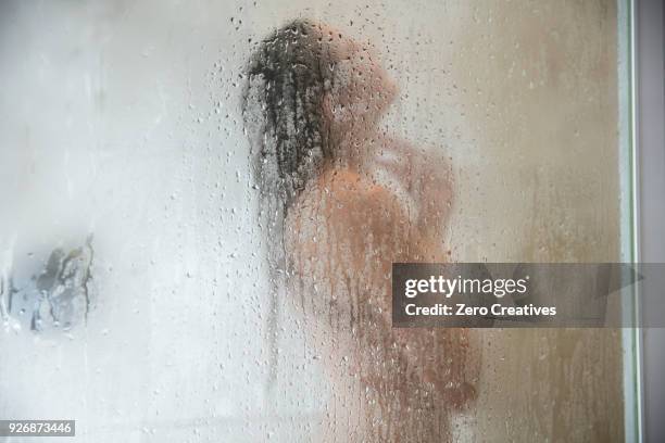 young woman in shower behind steamed glass door - duschen stock-fotos und bilder