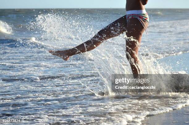 teenage girl standing in ocean kicking the water - ankle deep in water fotografías e imágenes de stock