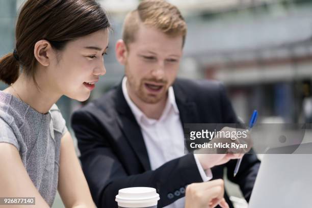 young businesswoman and man looking at laptop at sidewalk cafe - businesswoman in suit jackets stock-fotos und bilder