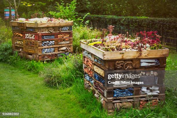 two large bug houses with several layers of different materials in a garden. - bug hotel stock pictures, royalty-free photos & images