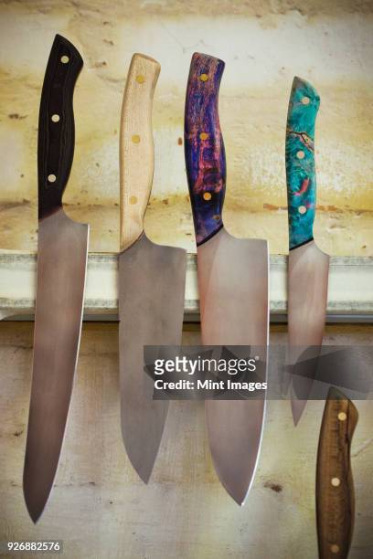 a selection of knives with shaped and painted wooden handles on a magnetic knife holder on a workshop wall. - magnetwand stock-fotos und bilder