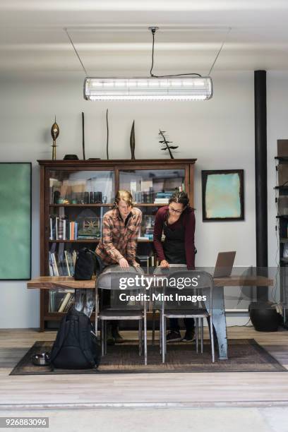 two women gathered around table in office area of a metal workshop, looking at technical blueprint. - the 2017 makers conference stock pictures, royalty-free photos & images