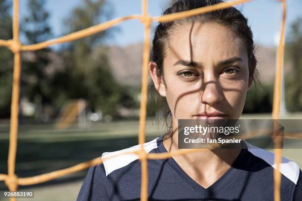 portrait of woman behind football goal netting looking at camera - fußball emotional stock-fotos und bilder
