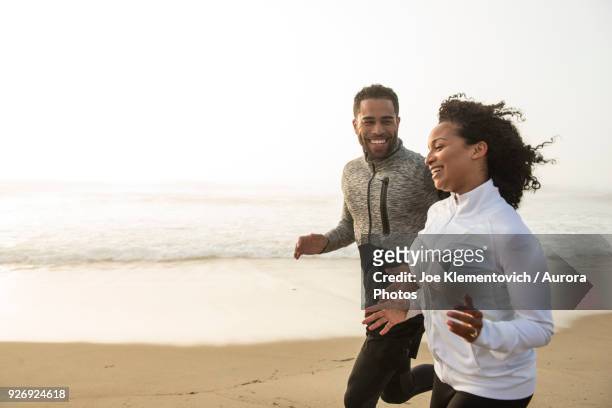man and woman jogging side by side on coastal beach and smiling, hampton, new hampshire, usa - vita attiva foto e immagini stock