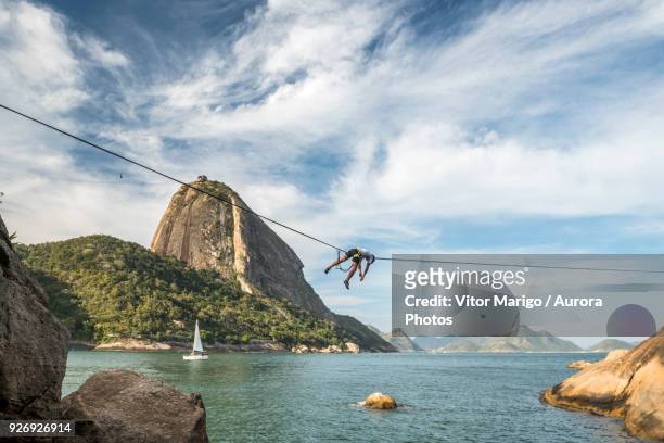 man lying on highline in contos de pescadores, vermelha beach, rio de janeiro, brazil - waterline stock pictures, royalty-free photos & images