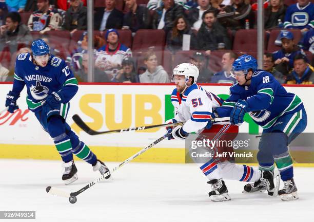 Ben Hutton of the Vancouver Canucks looks on as teammate Jake Virtanen checks David Desharnais of the New York Rangers during their NHL game at...