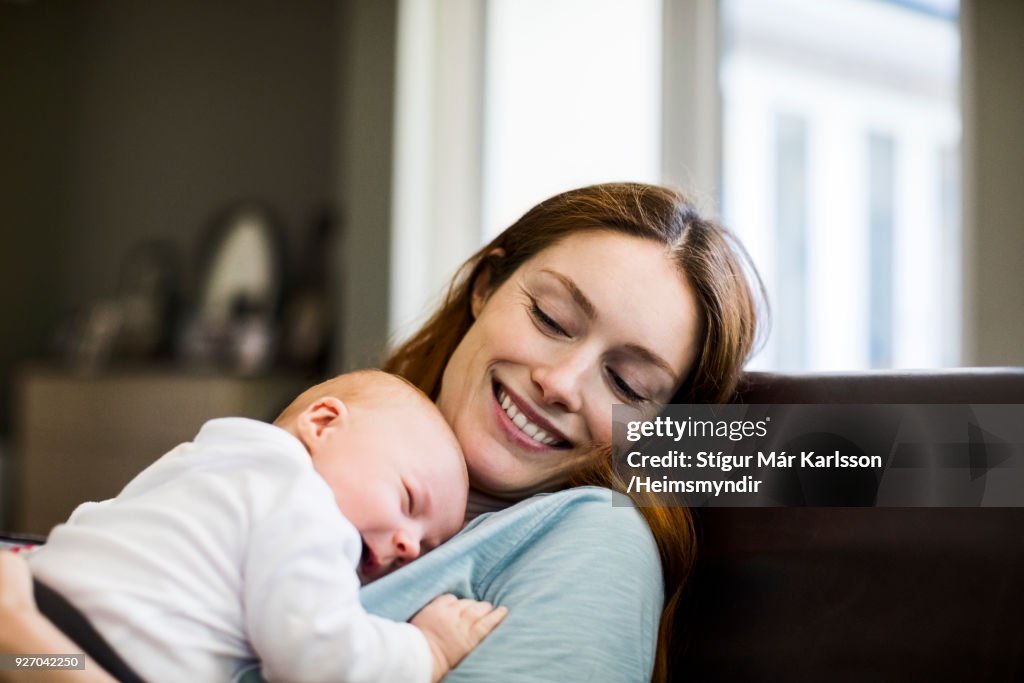 Smiling mother with sleeping newborn son on sofa