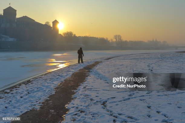 Man walks in front of Wawel Castle during a sunrise along the edge of a partially frozen section of Vistula river in Krakow, as icy weather continues...