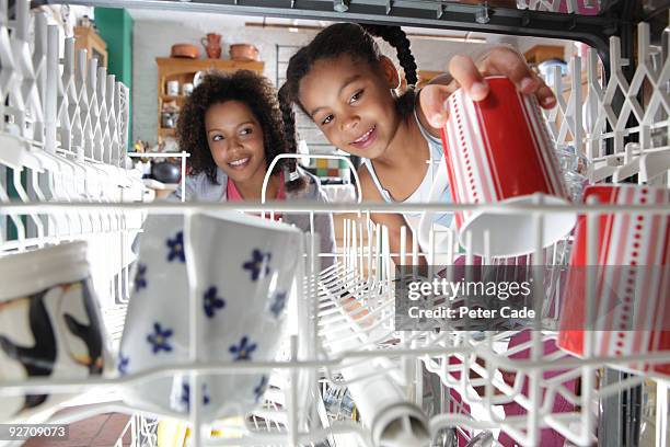 mother and daughter loading dishwasher - spülmaschine stock-fotos und bilder